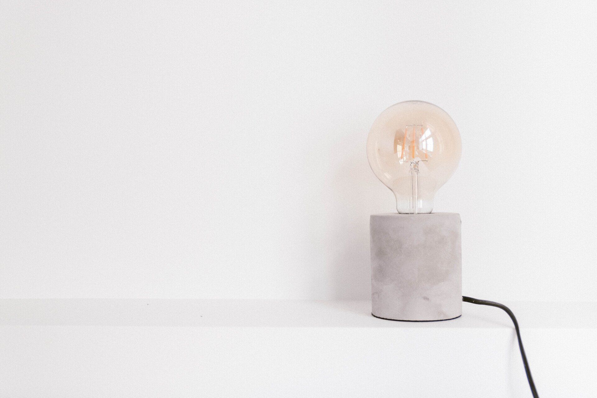 A light bulb is sitting on a concrete base on a white shelf.