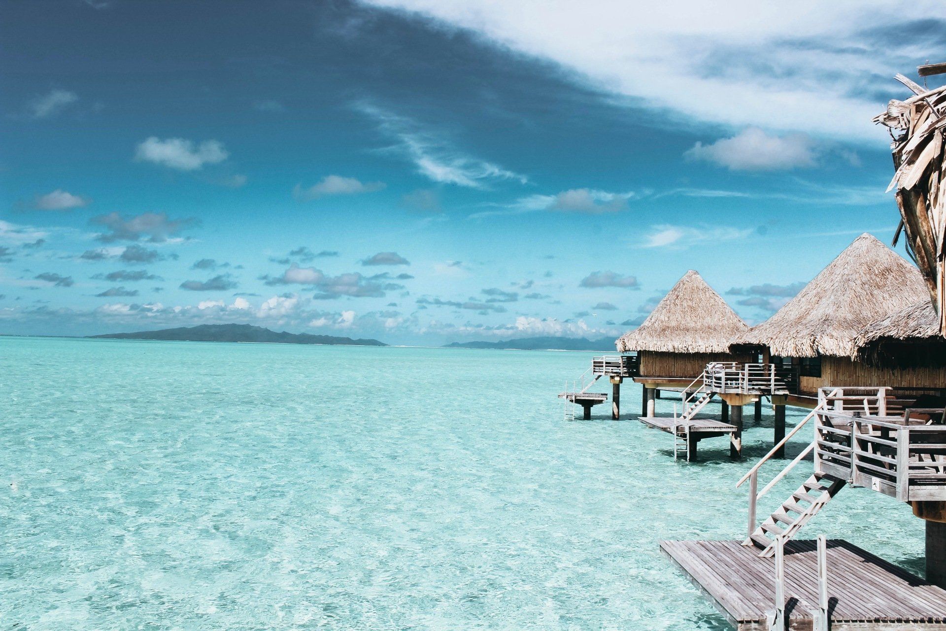 A row of thatched huts on stilts in the middle of the ocean. Vacation Travel Exclusives