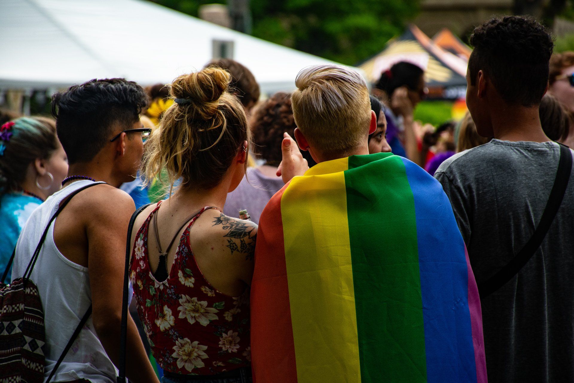 a group of people standing in a crowd with a rainbow flag .