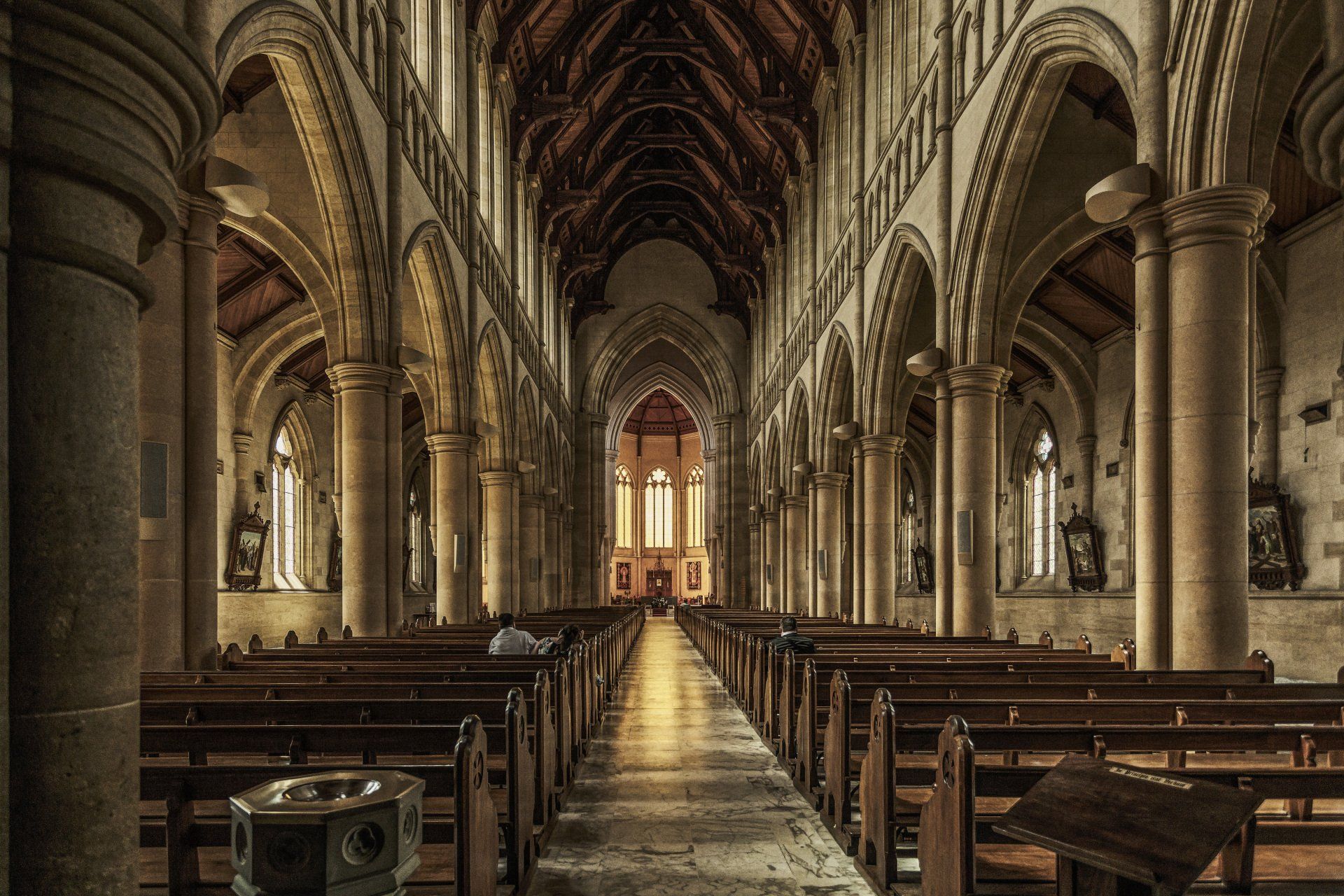 The inside of a church with rows of wooden benches and columns.