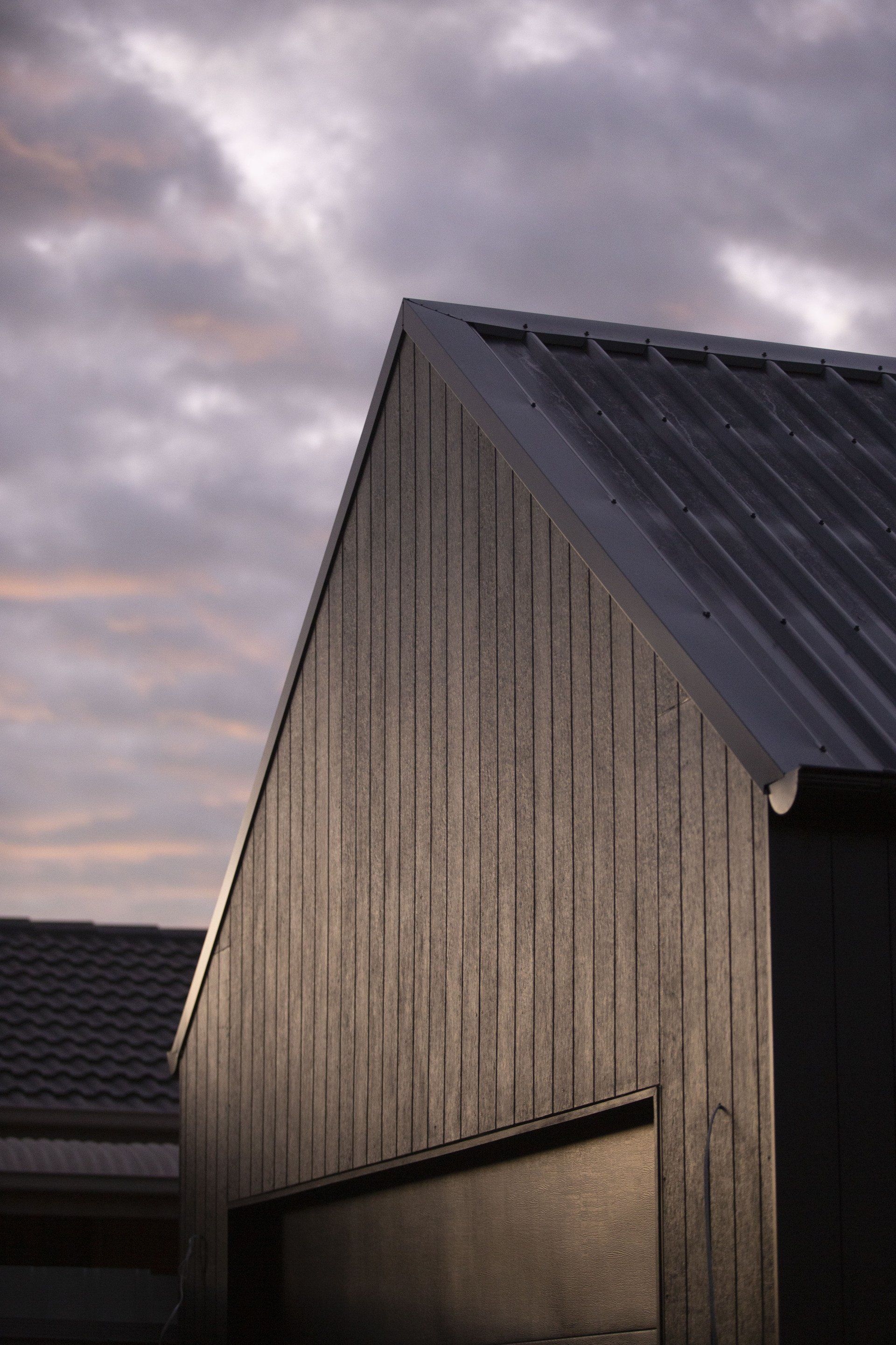 Black wooden building with angled roof against a cloudy sky.