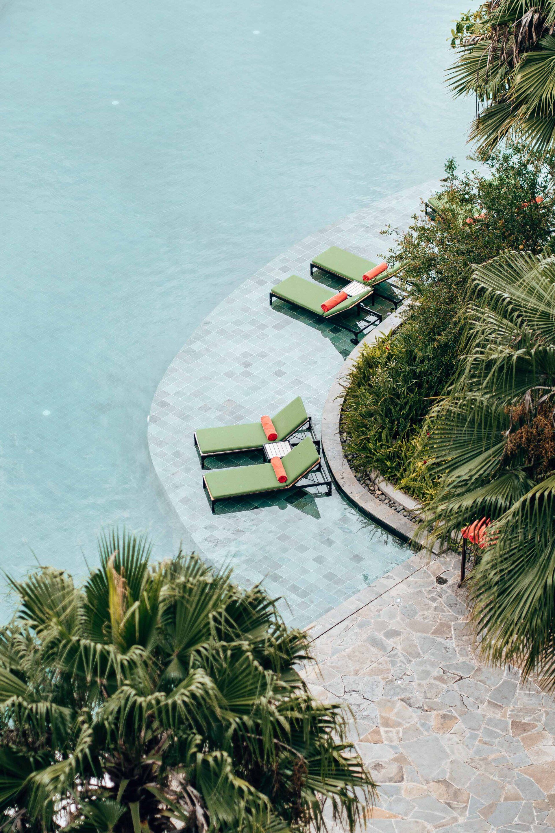 A swimming pool surrounded by palm trees and chairs.