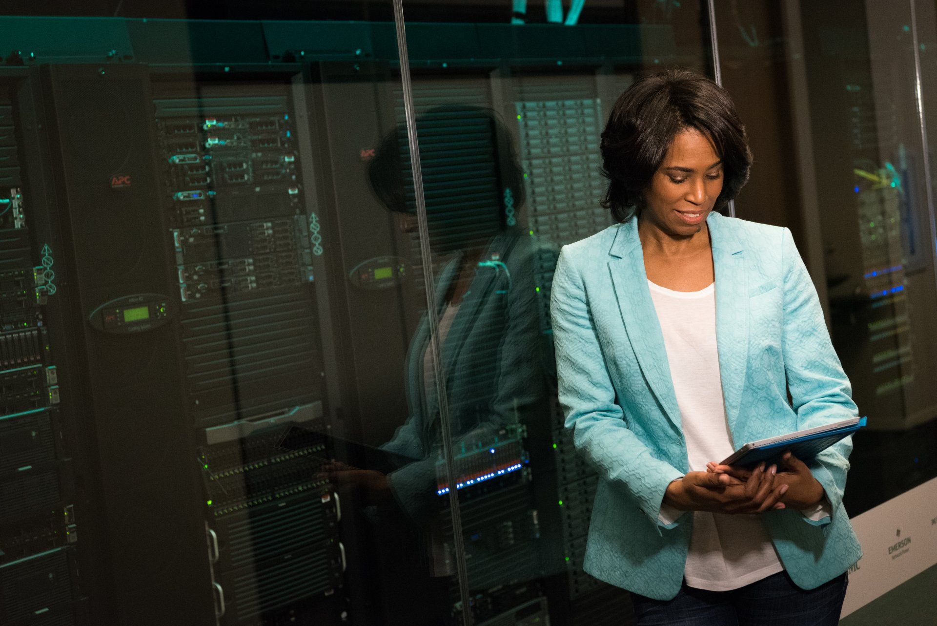 a woman in a blue jacket is holding a tablet in a server room .