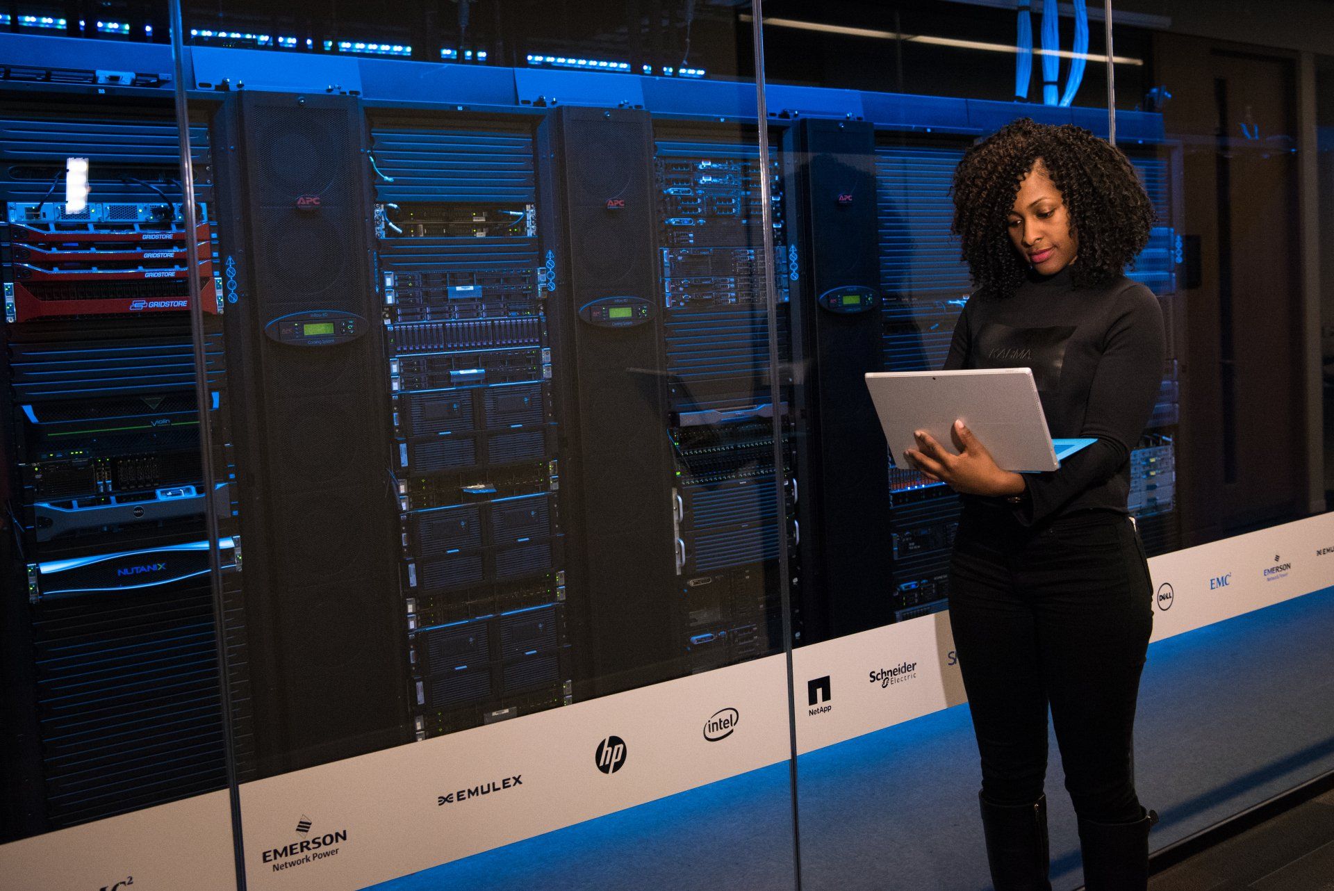 a woman is standing in a server room holding a laptop
