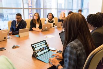 A group of people are sitting around a table with laptops.