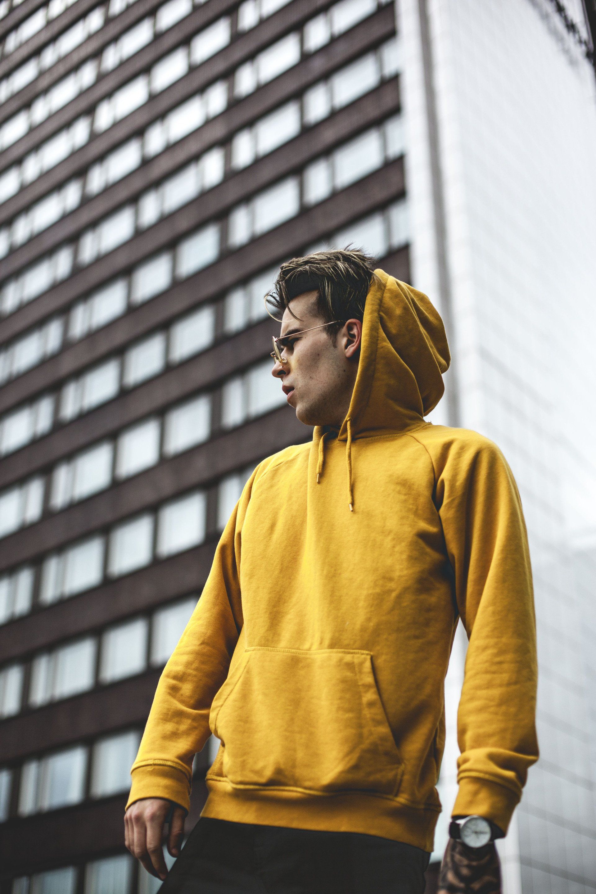 A man wearing a yellow hoodie is standing in front of a tall building.