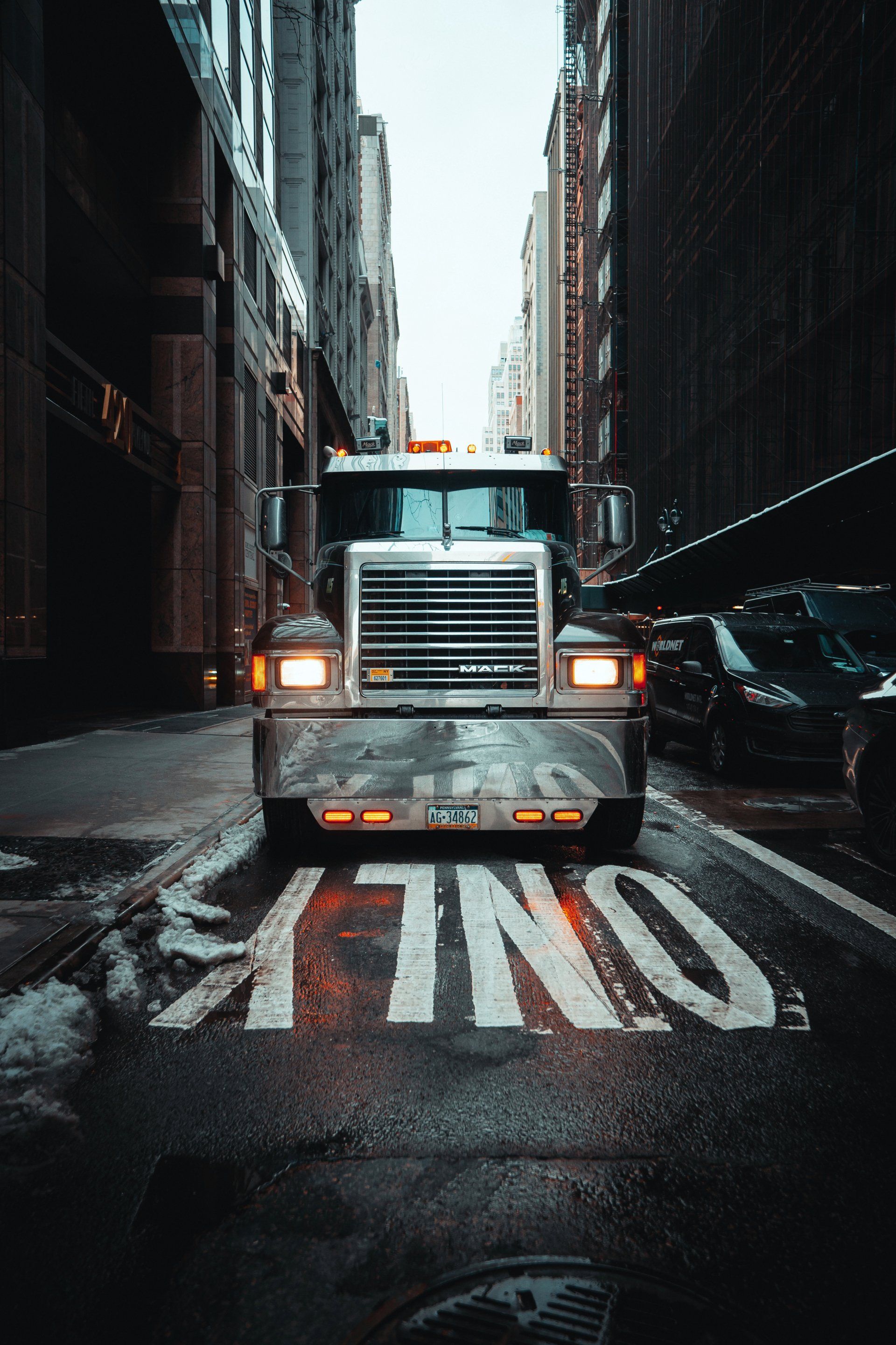 The front of a semi sitting at a crosswalk in a city. 