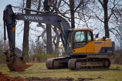 A yellow and gray volvo excavator is parked in a field.