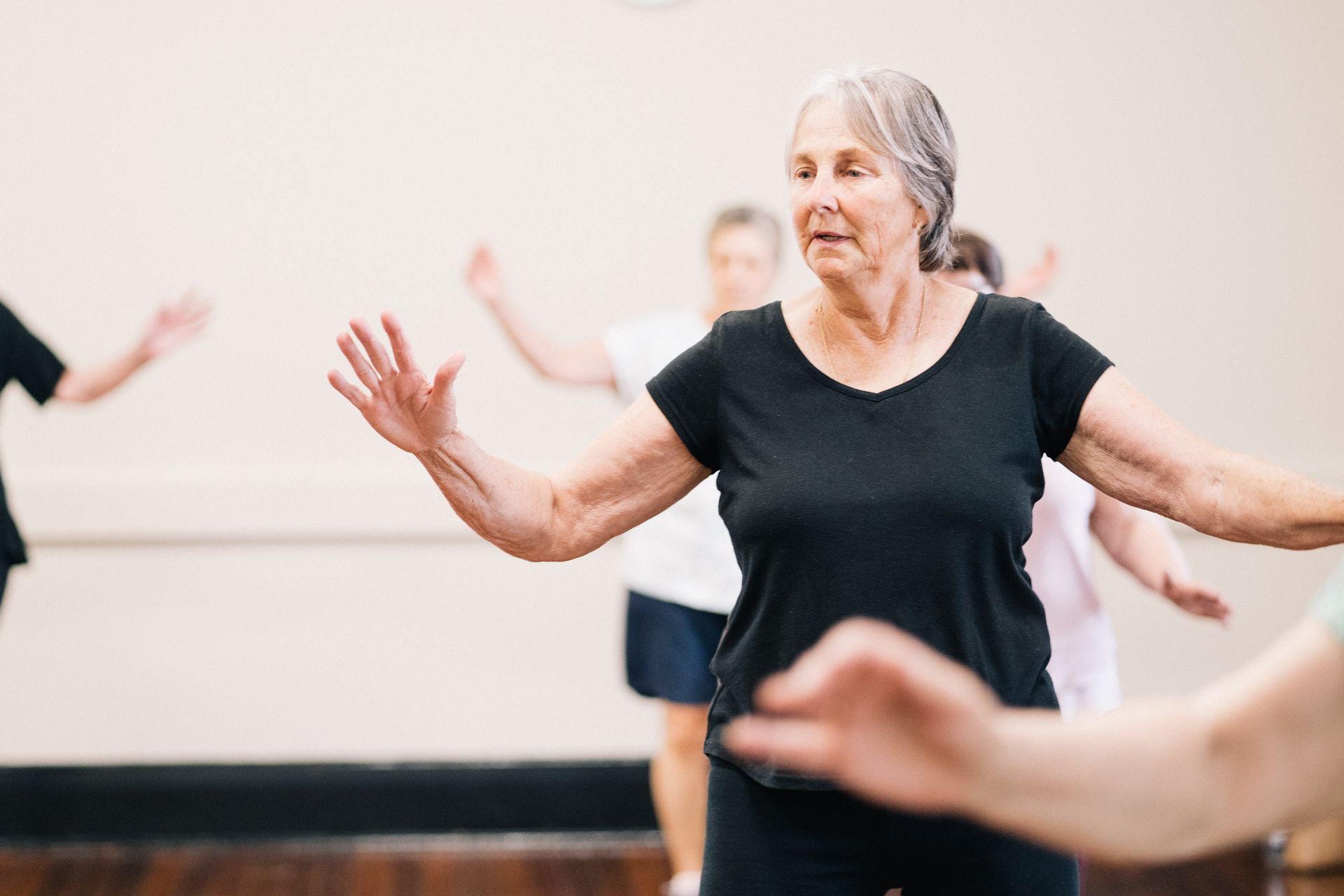 Woman in black shirt leading exercise class, arms outstretched.