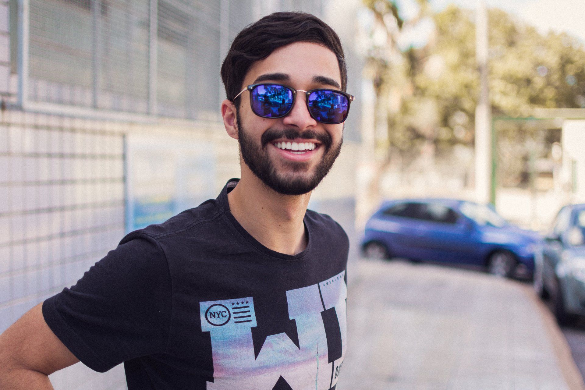 A man with a beard wearing sunglasses and a black shirt is smiling.