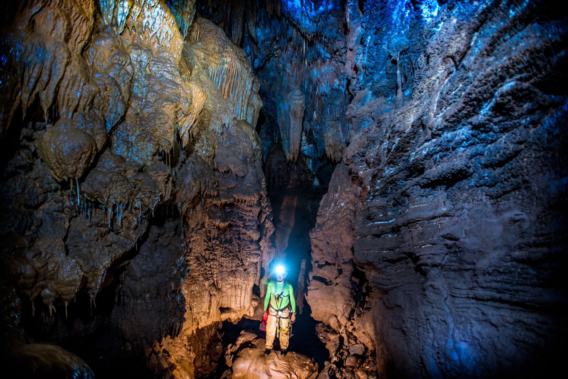 A man is standing in a cave with a light on his head.