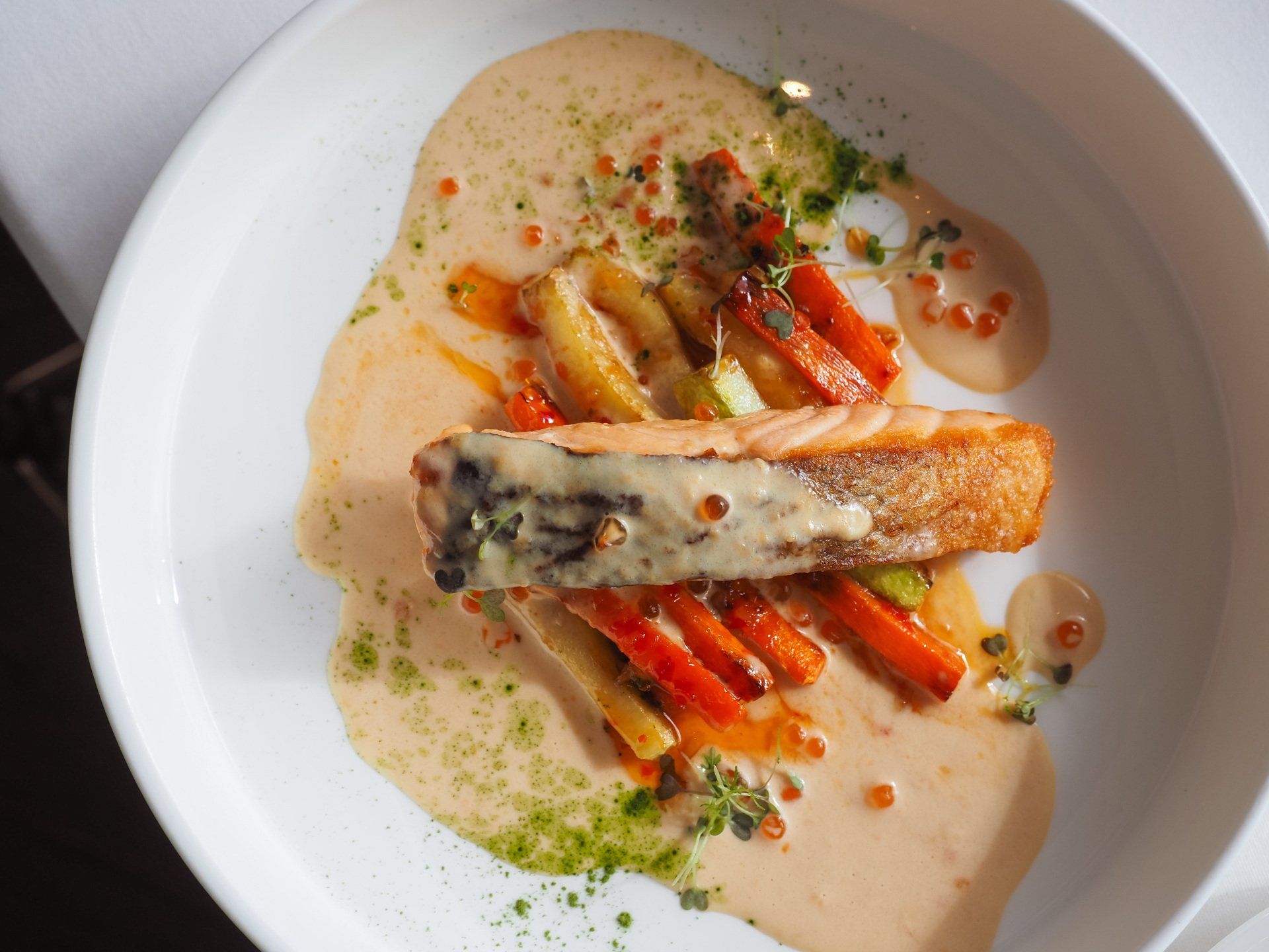 Une assiette blanche surmontée d'un morceau de saumon et de carottes.