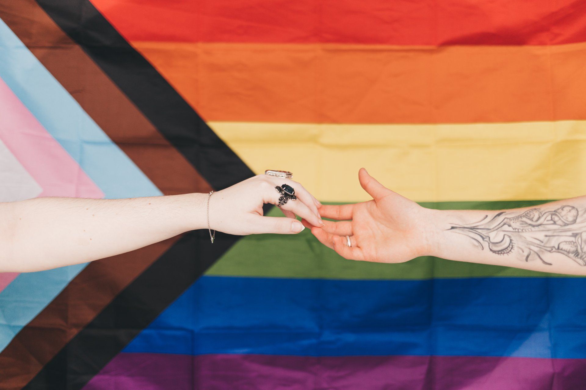LGBTIQA+Flag and hands reaching towards eachother
