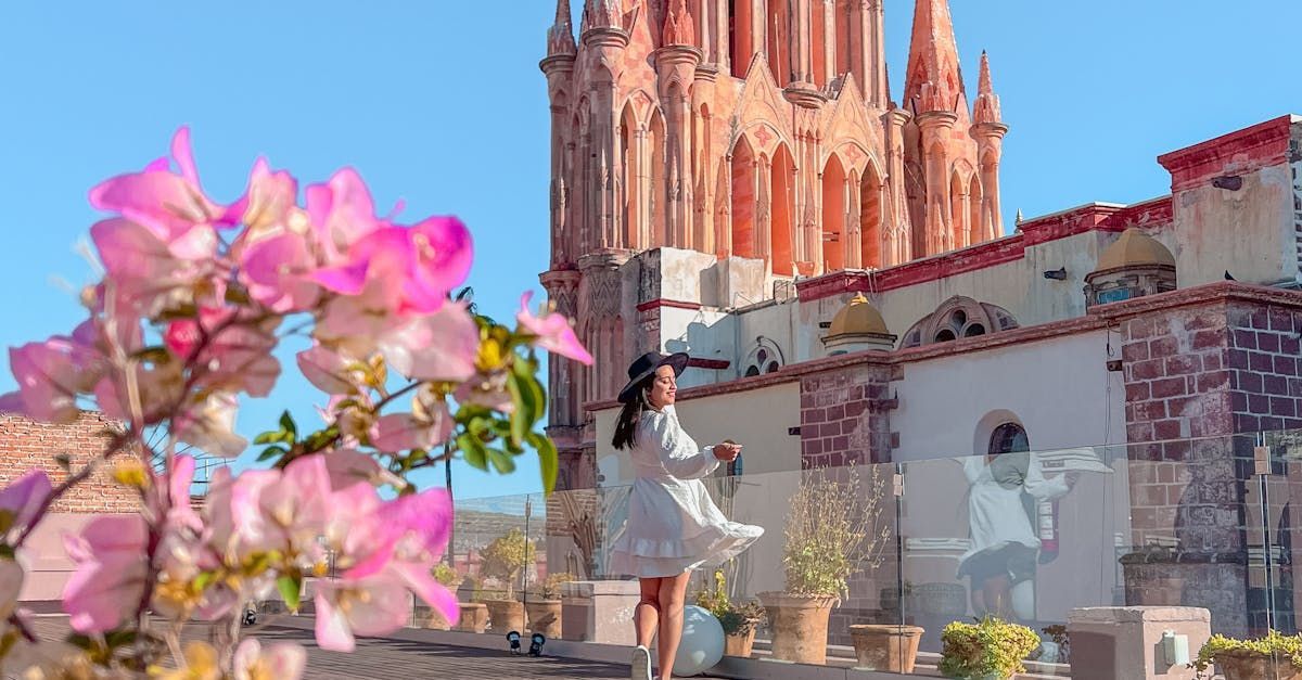 Una mujer con un vestido blanco está parada frente a una iglesia rodeada de flores rosas.