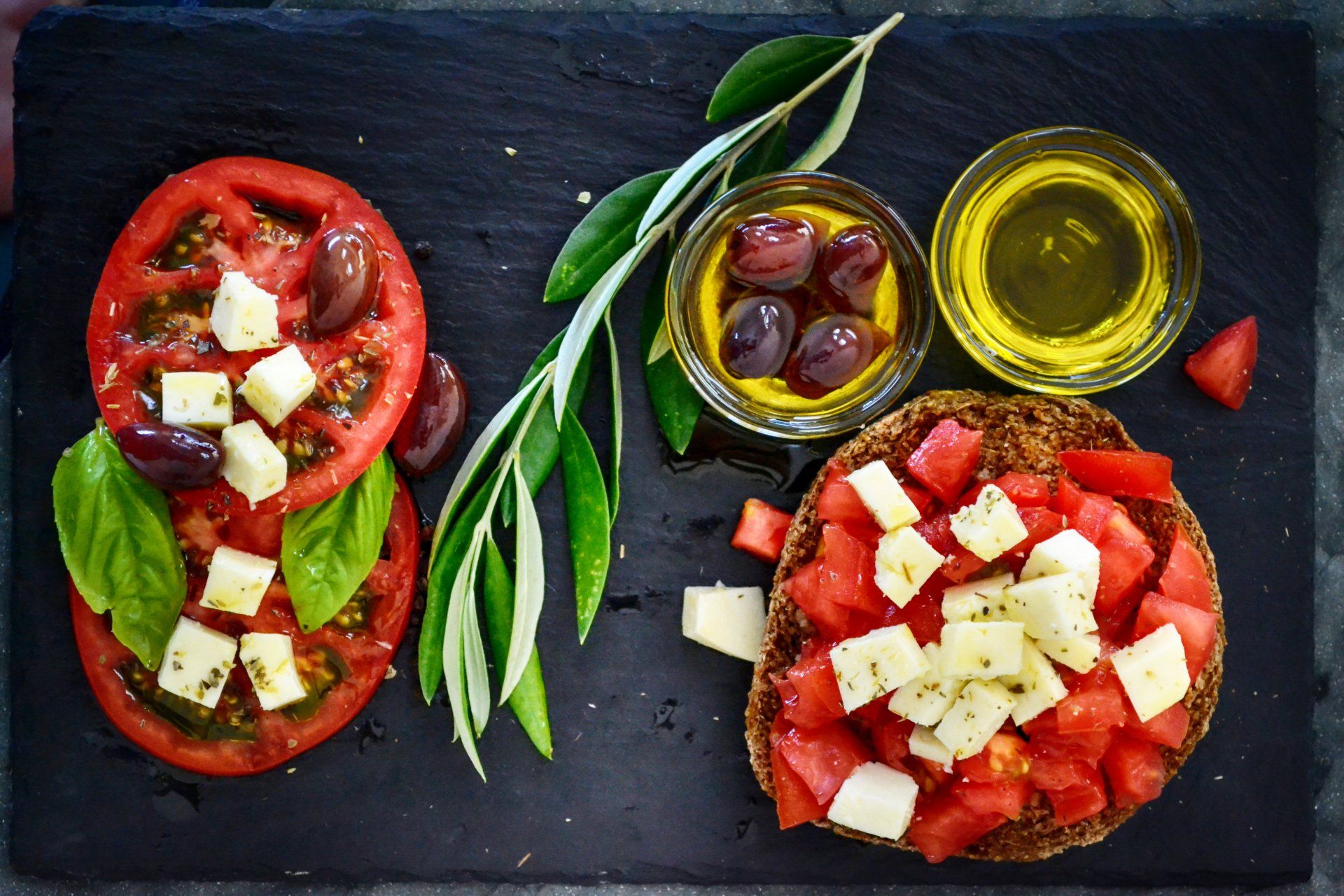 A plate of food with tomatoes , olives , cheese and basil on a table.
