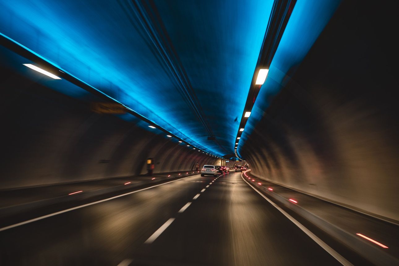 A car is driving through a tunnel with blue lights on the ceiling.