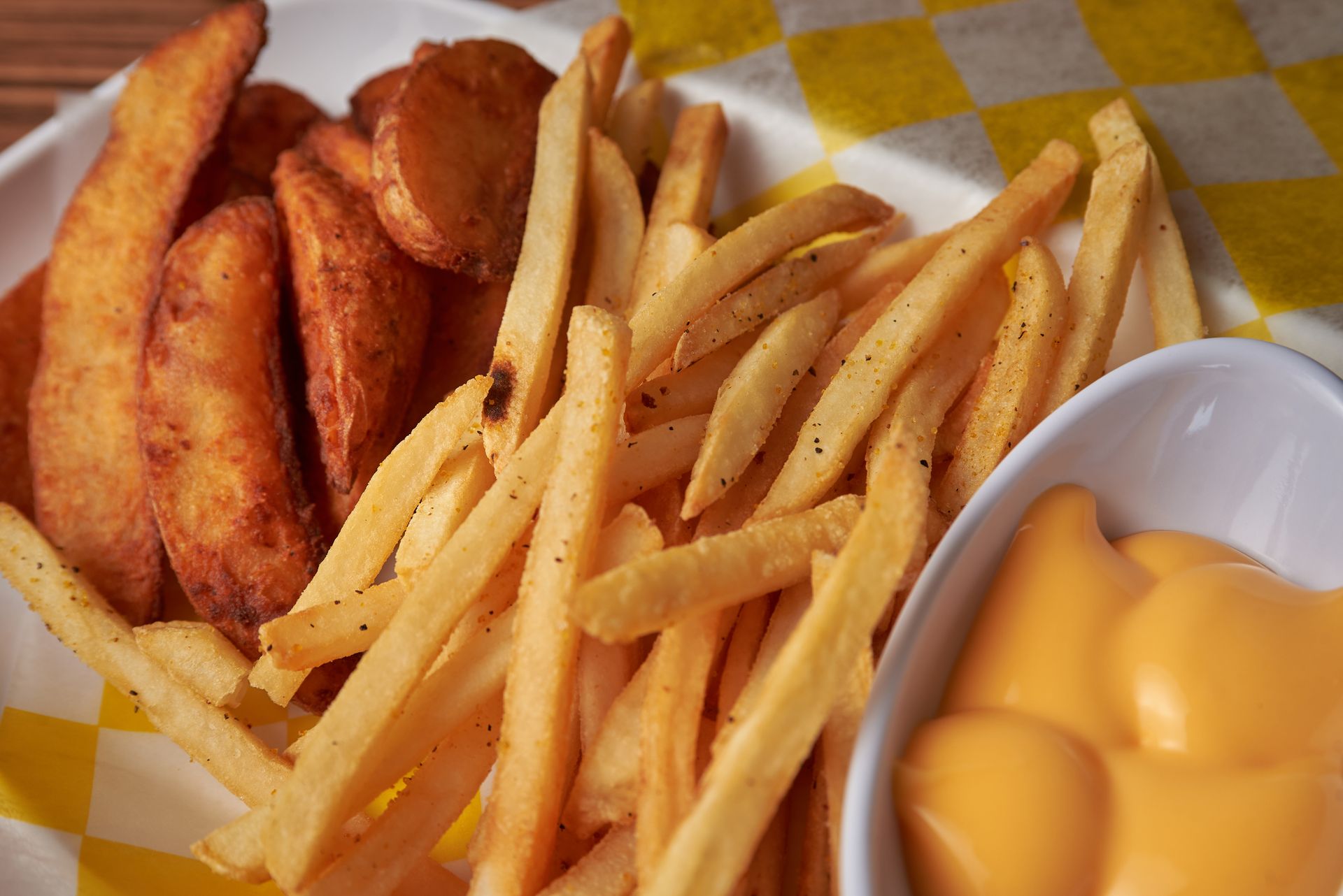 A plate of french fries and wedges with a bowl of cheese sauce.