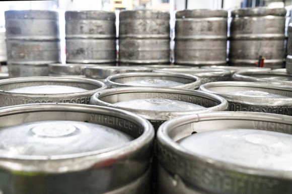 A bunch of beer kegs are stacked on top of each other in a warehouse.