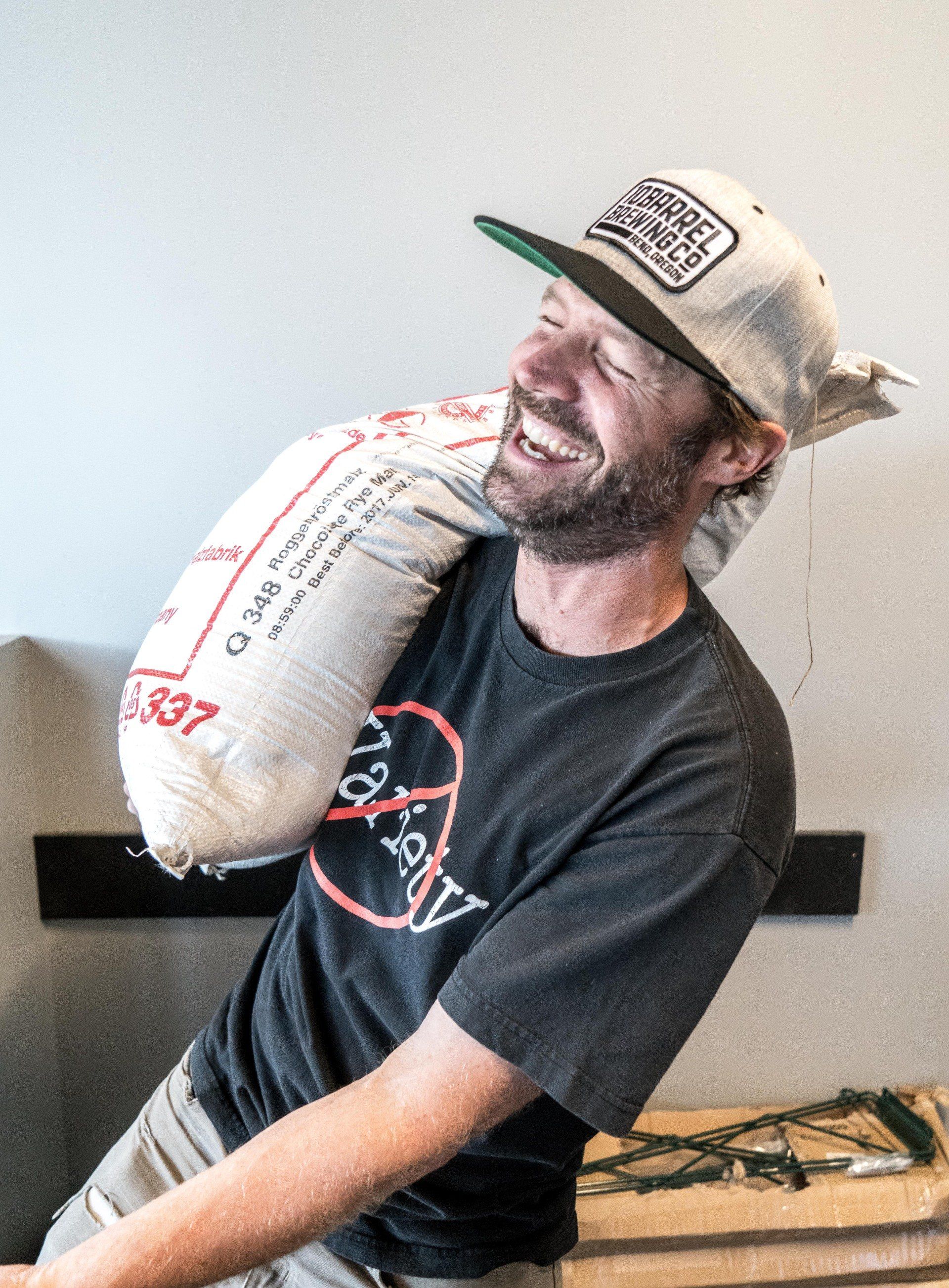 A man wearing a hat is carrying a large bag on his shoulder.