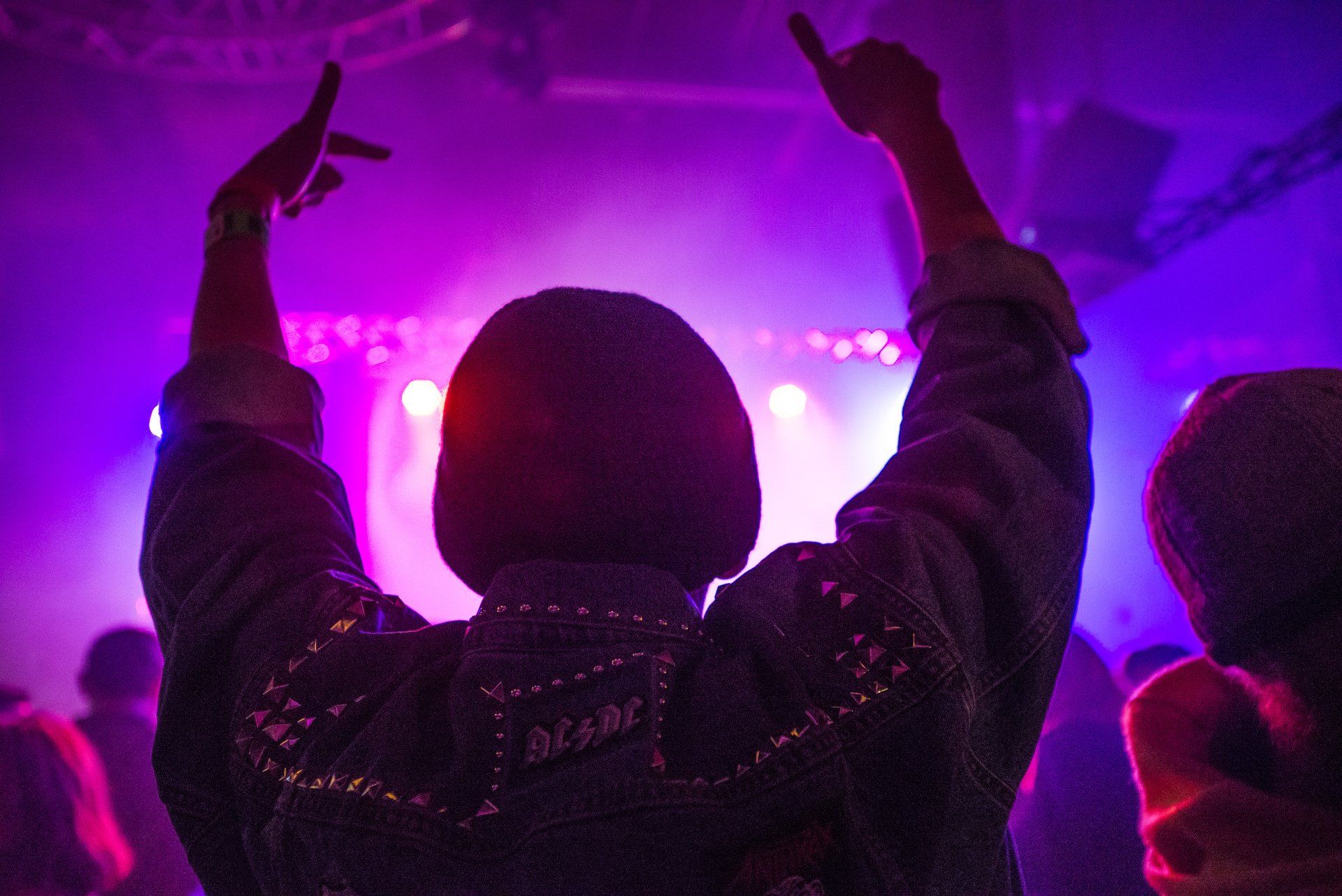 A person is standing in front of a stage with their arms in the air.