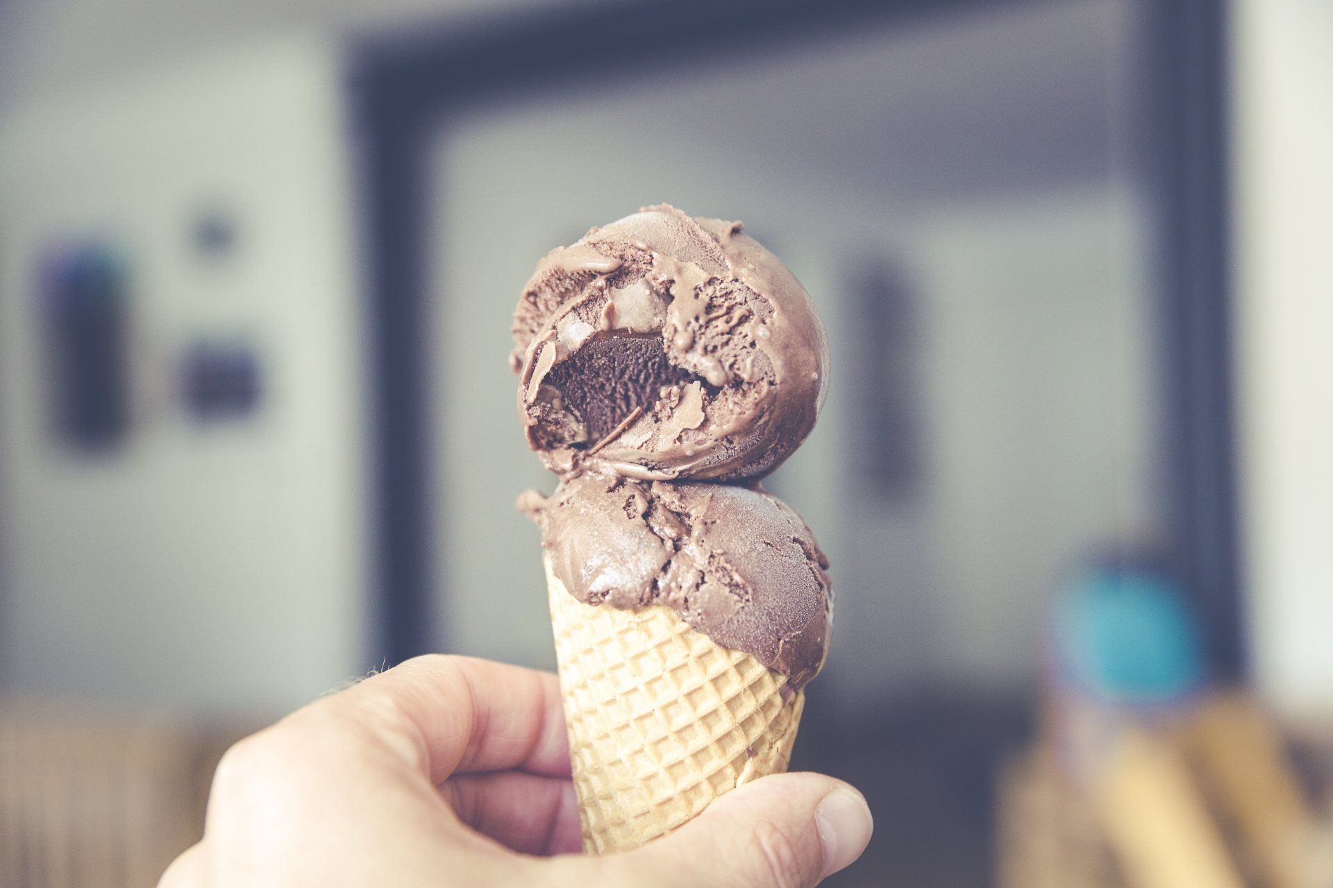 A person is holding two scoops of chocolate ice cream in a waffle cone.