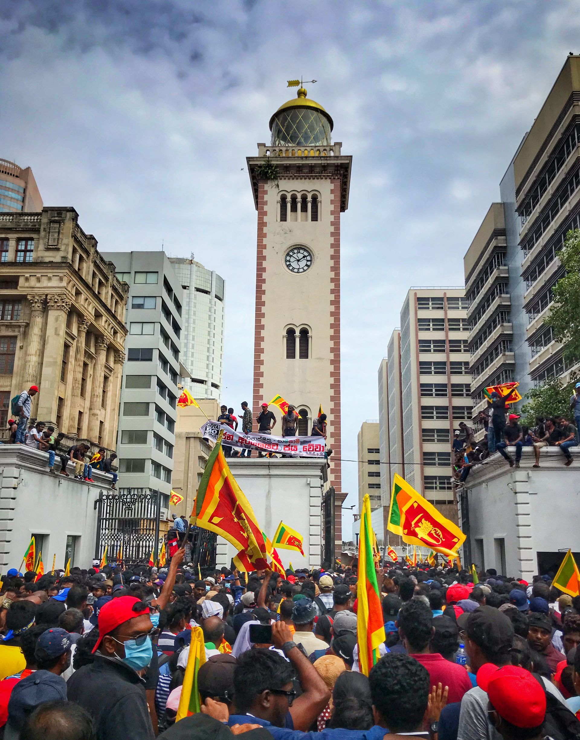 A crowd of people are gathered in front of a clock tower in a city.
