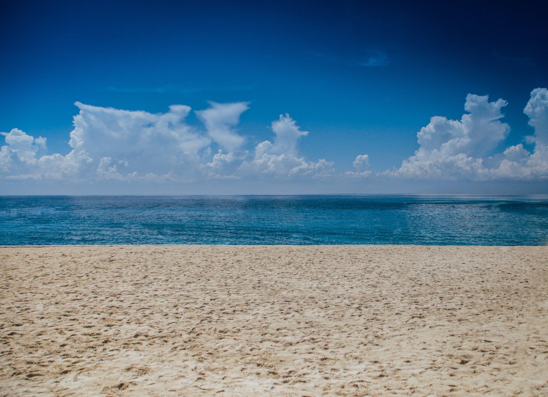 Una playa vacía con el océano al fondo y un cielo azul con nubes.