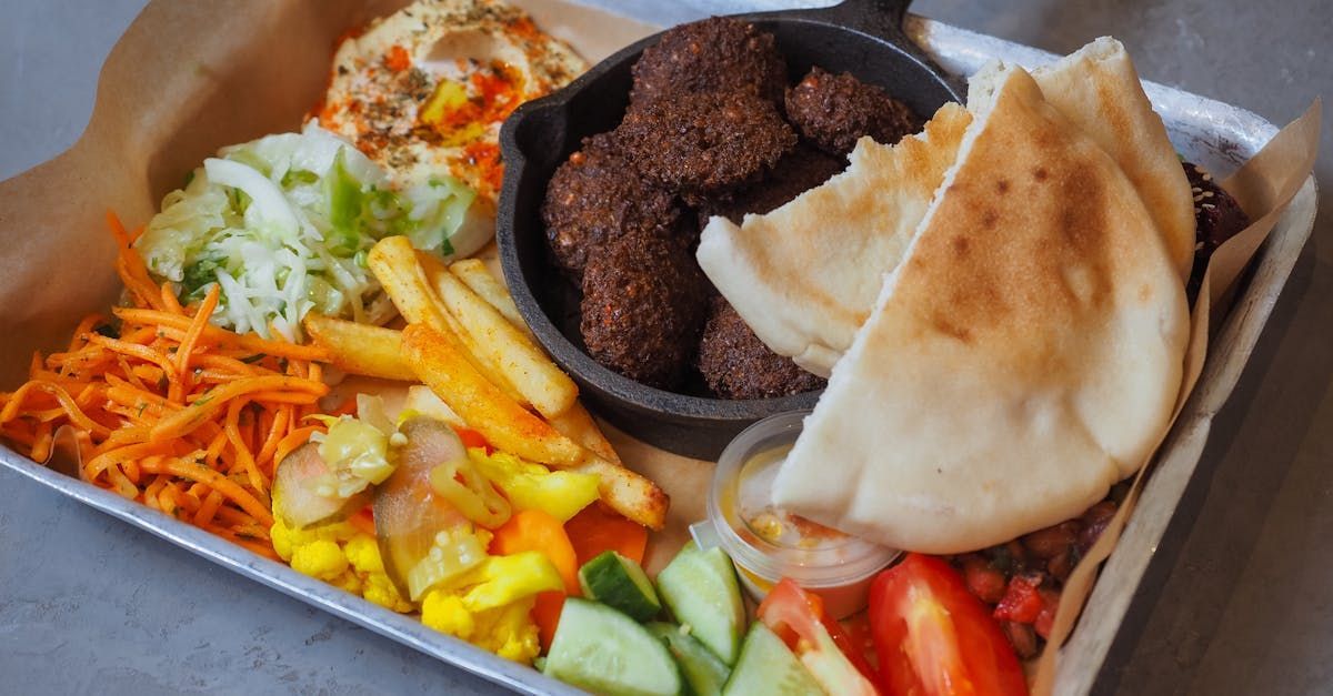 A tray of food with falafel , pita bread , french fries and vegetables on a table.