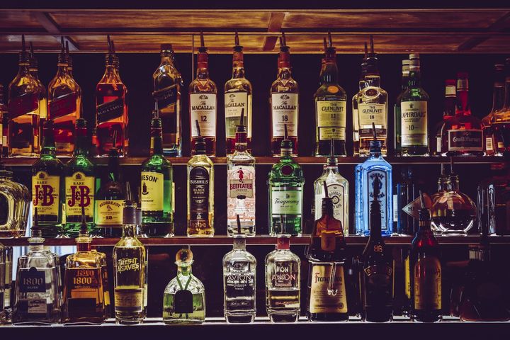 A row of bottles of liquor are lined up on a shelf in a bar.