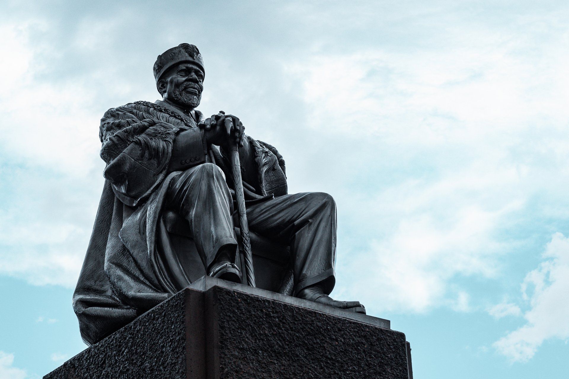 A statue of a man sitting on top of a rock holding a cane.