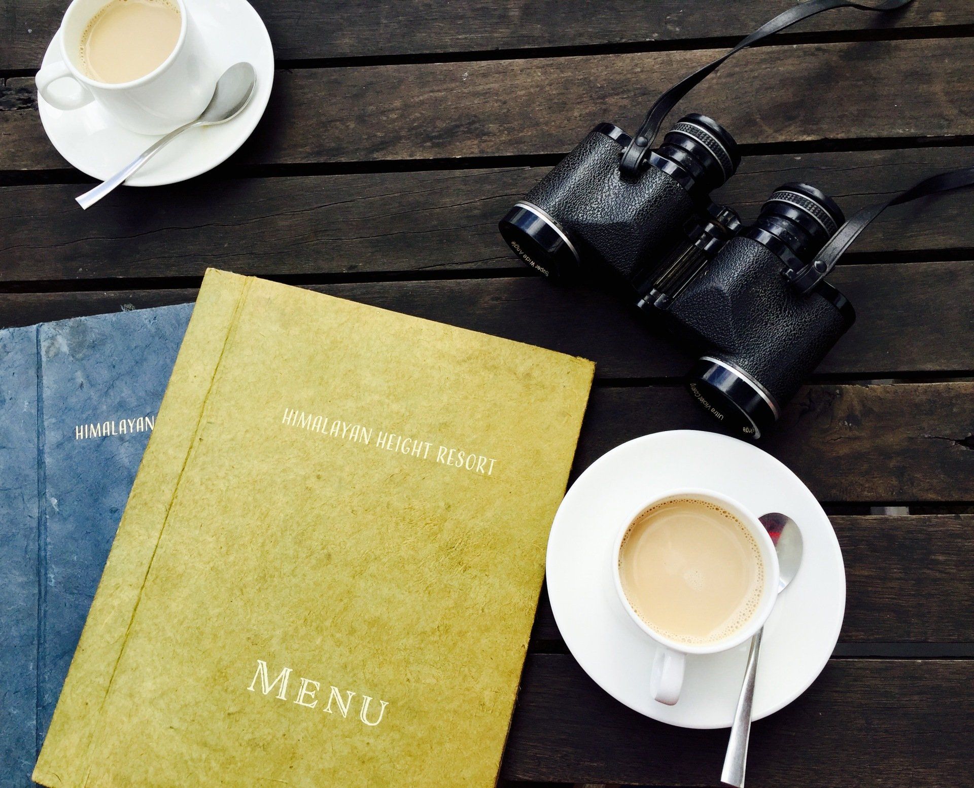 a menu is on a table next to a cup of coffee and binoculars