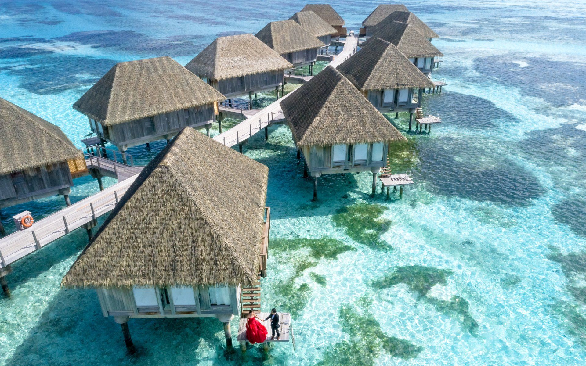 An aerial view of a row of thatched huts in the middle of the ocean.