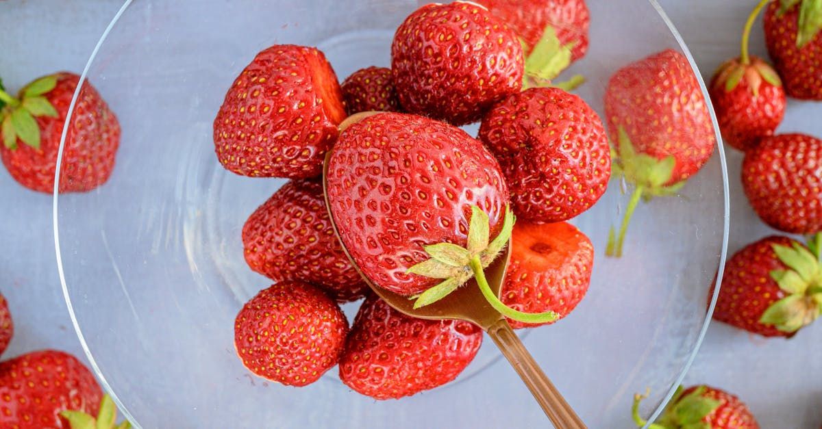 Strawberries are sitting on a glass plate with a spoon.