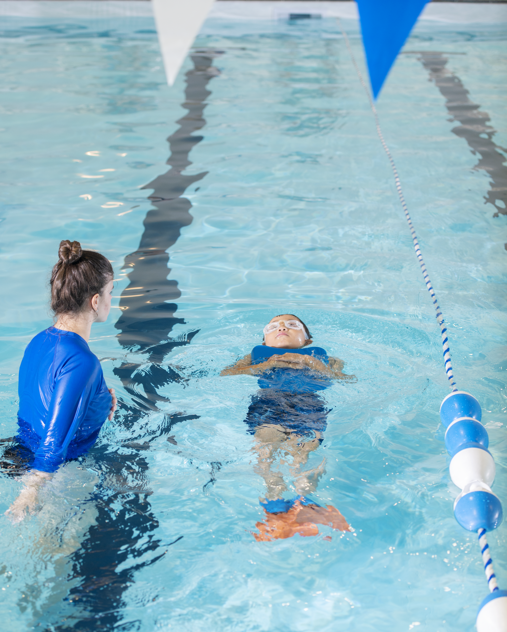 A woman is teaching a child how to swim in a swimming pool.