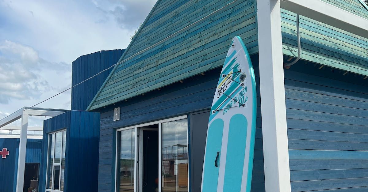 A blue surfboard is leaning against a blue building.