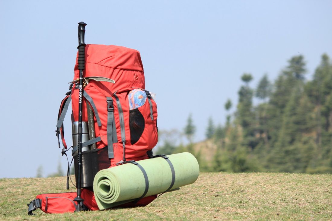 Ein roter Rucksack liegt auf einem grasbedeckten Feld.