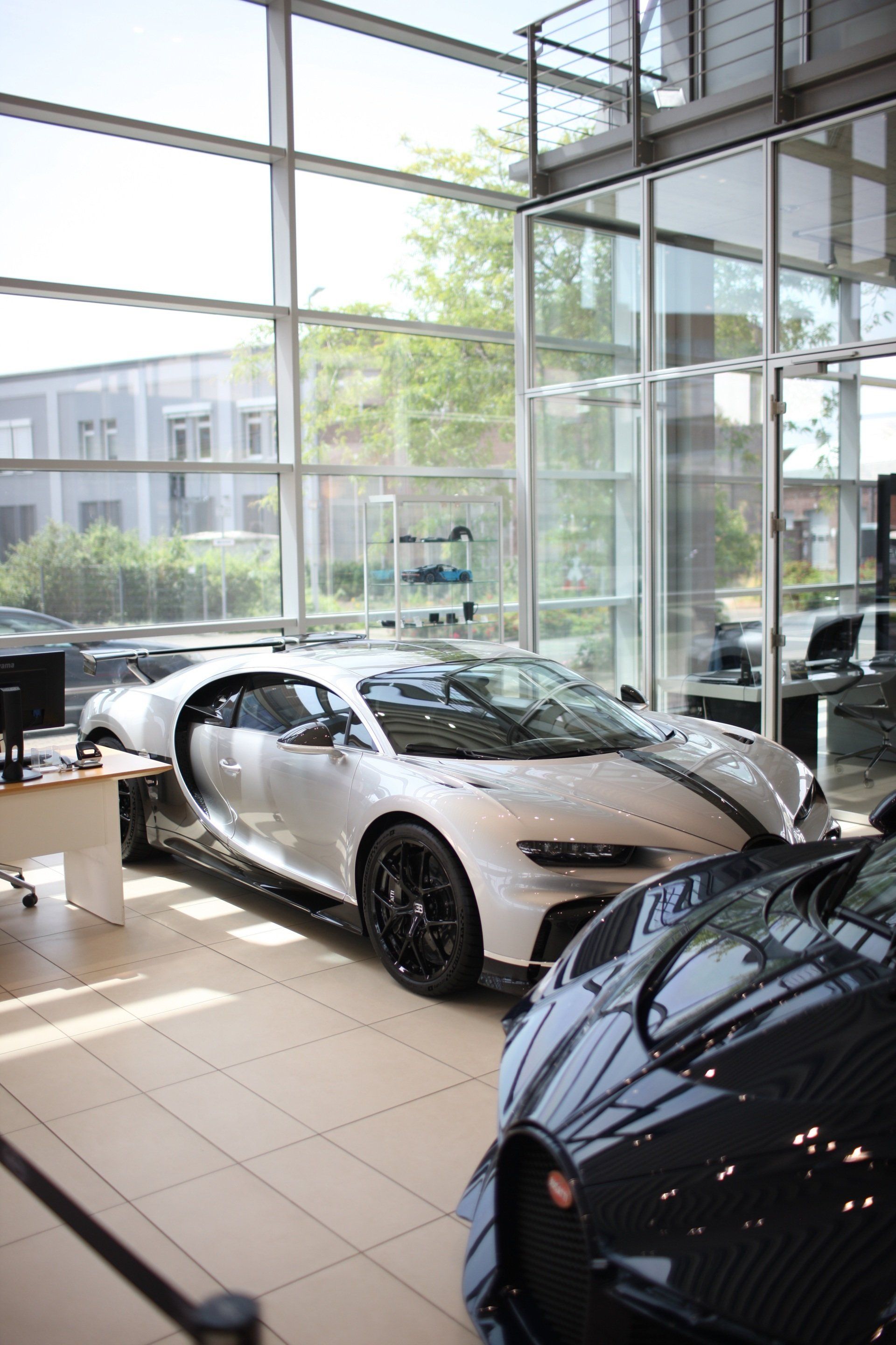 A white sports car is parked in a showroom next to a black sports car.
