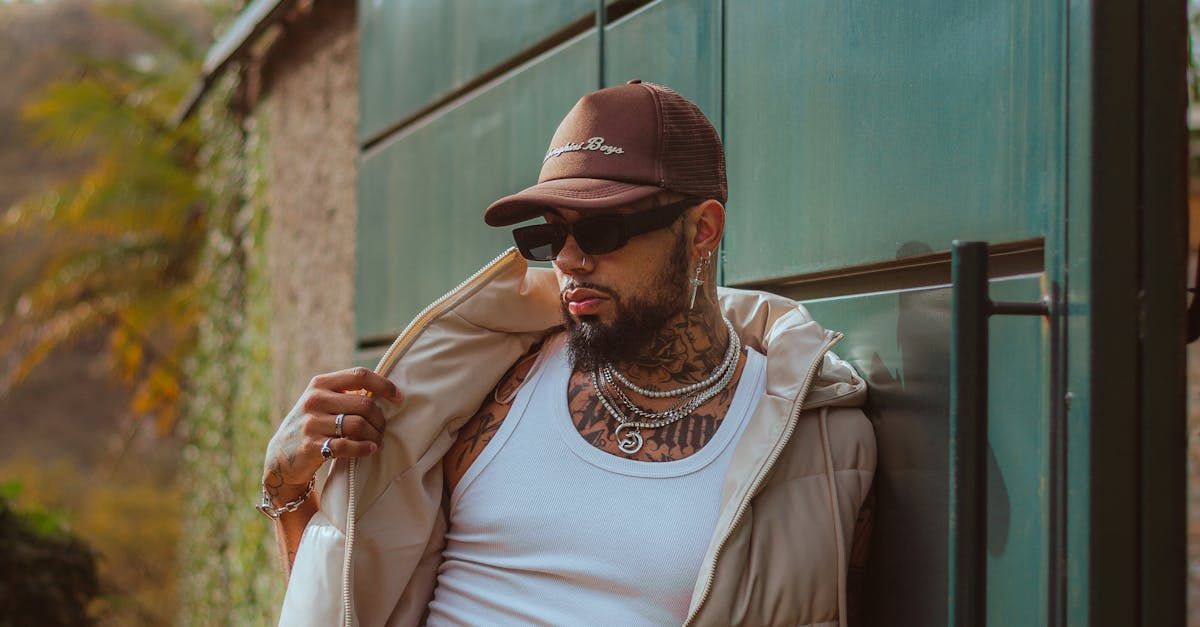 A man wearing a hat and sunglasses is leaning against a wall.