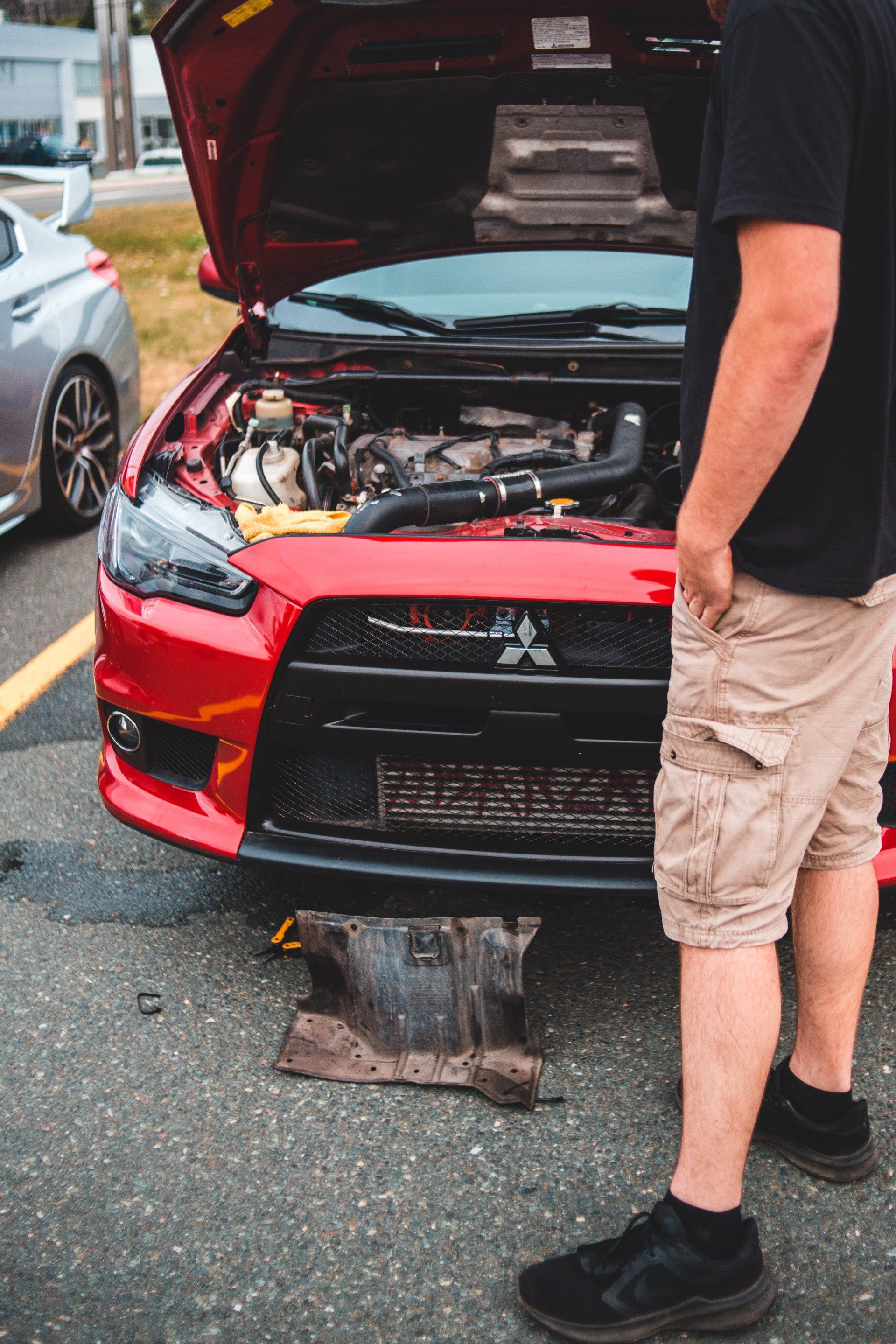 A man is standing in front of a red car with the hood open.