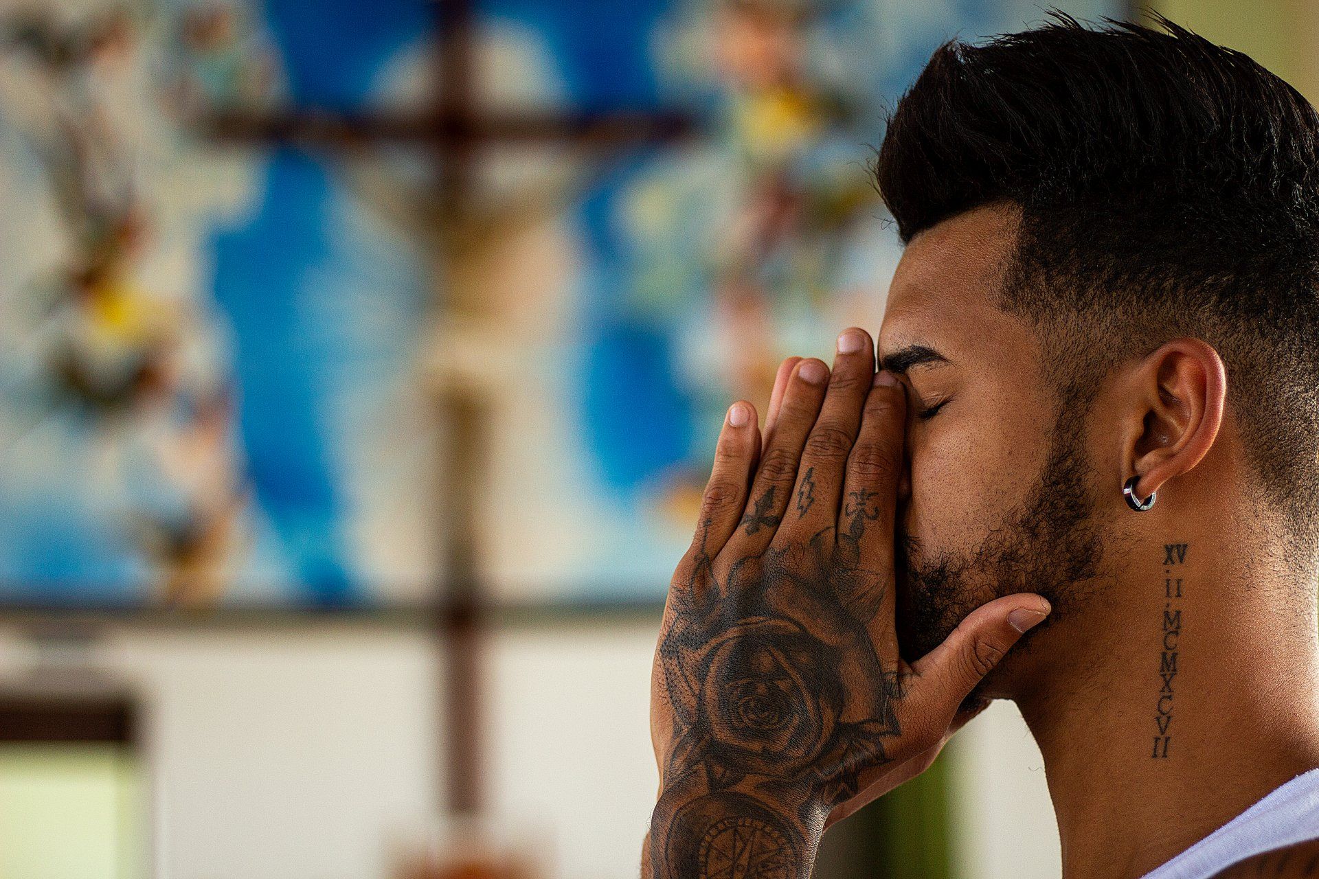 A man with a tattoo on his neck is praying in front of a cross.