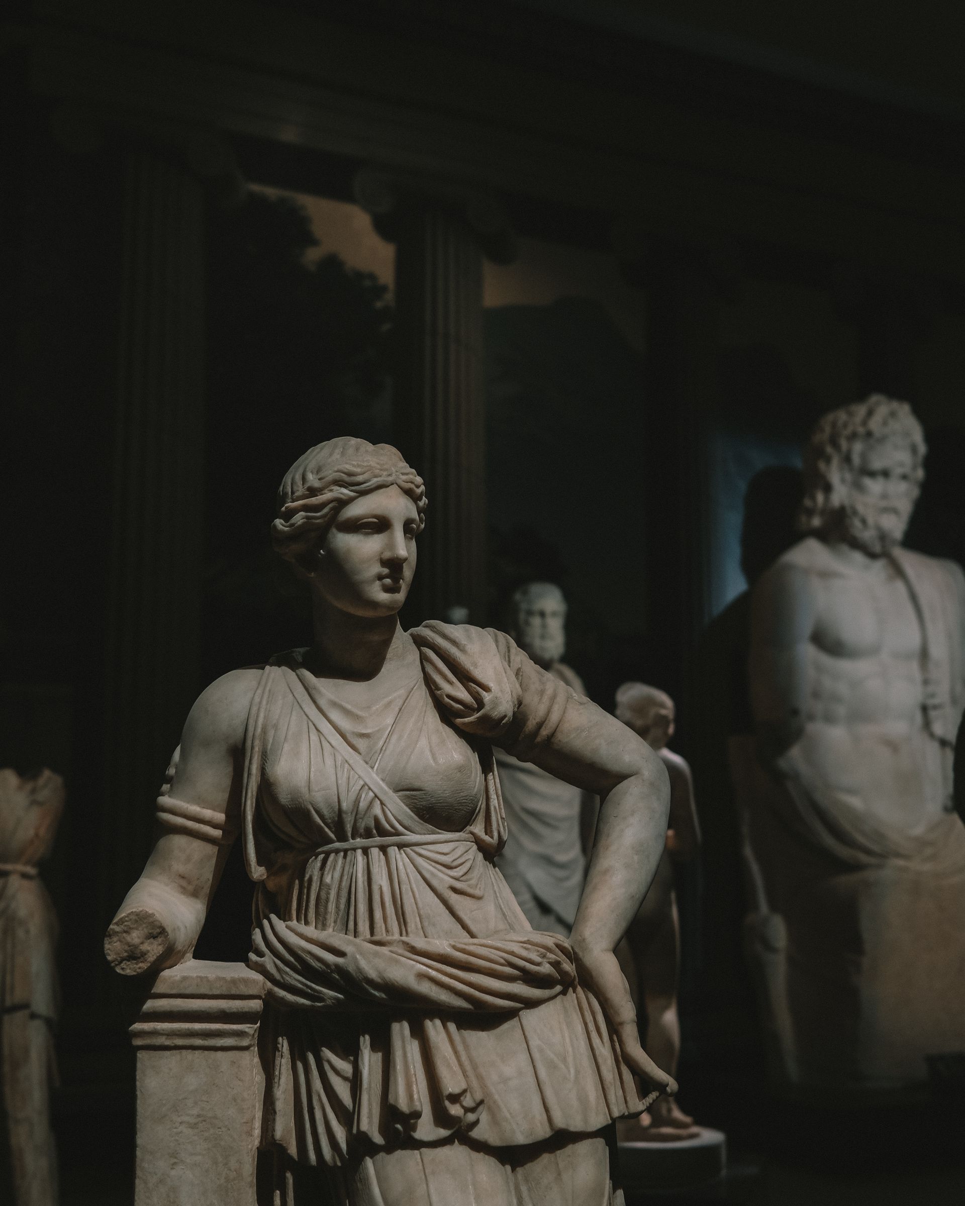 A statue of a woman sitting on a pillar in a dark room.