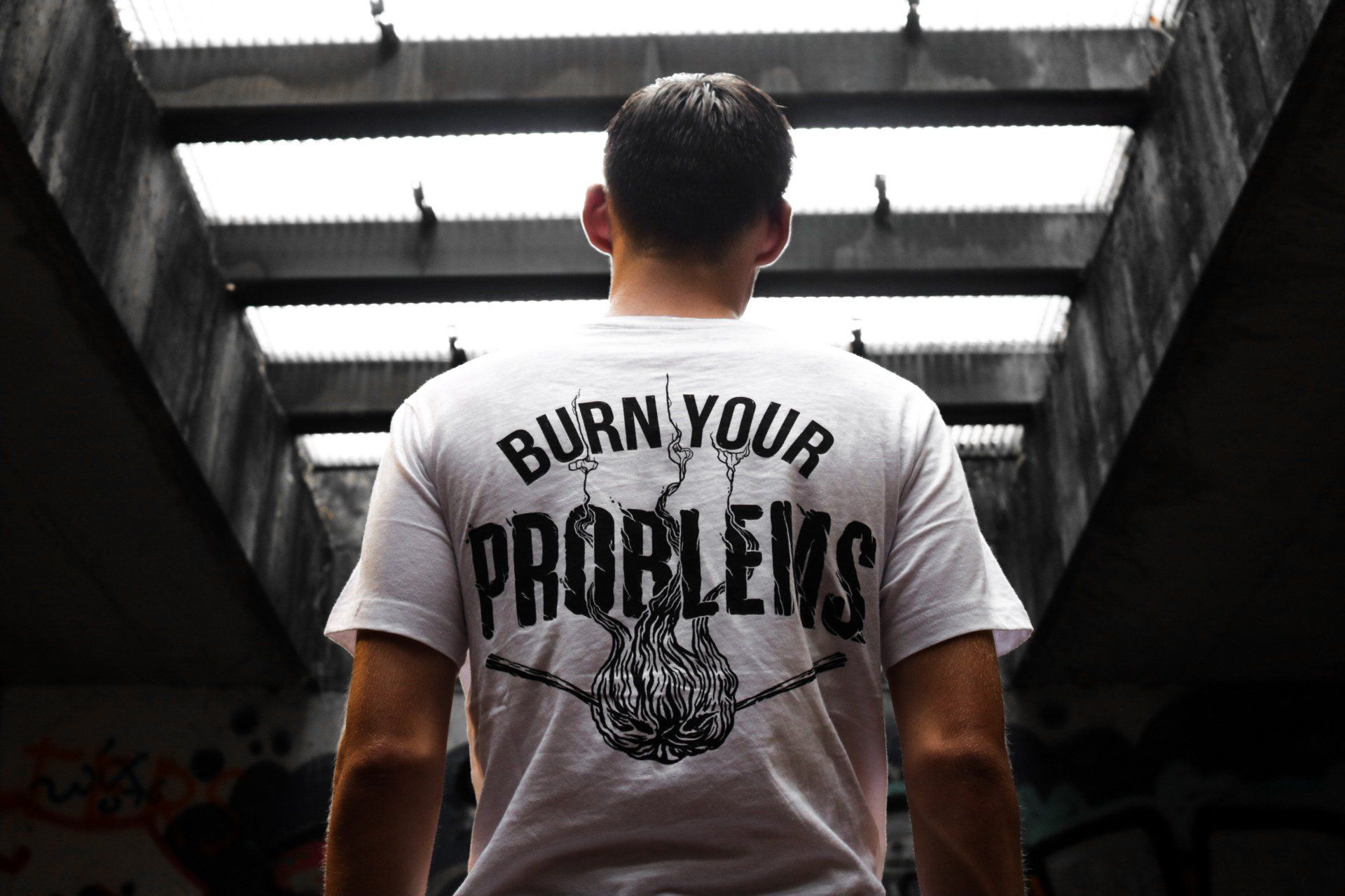 A man is wearing a white t-shirt that says `` burn your problems ''.