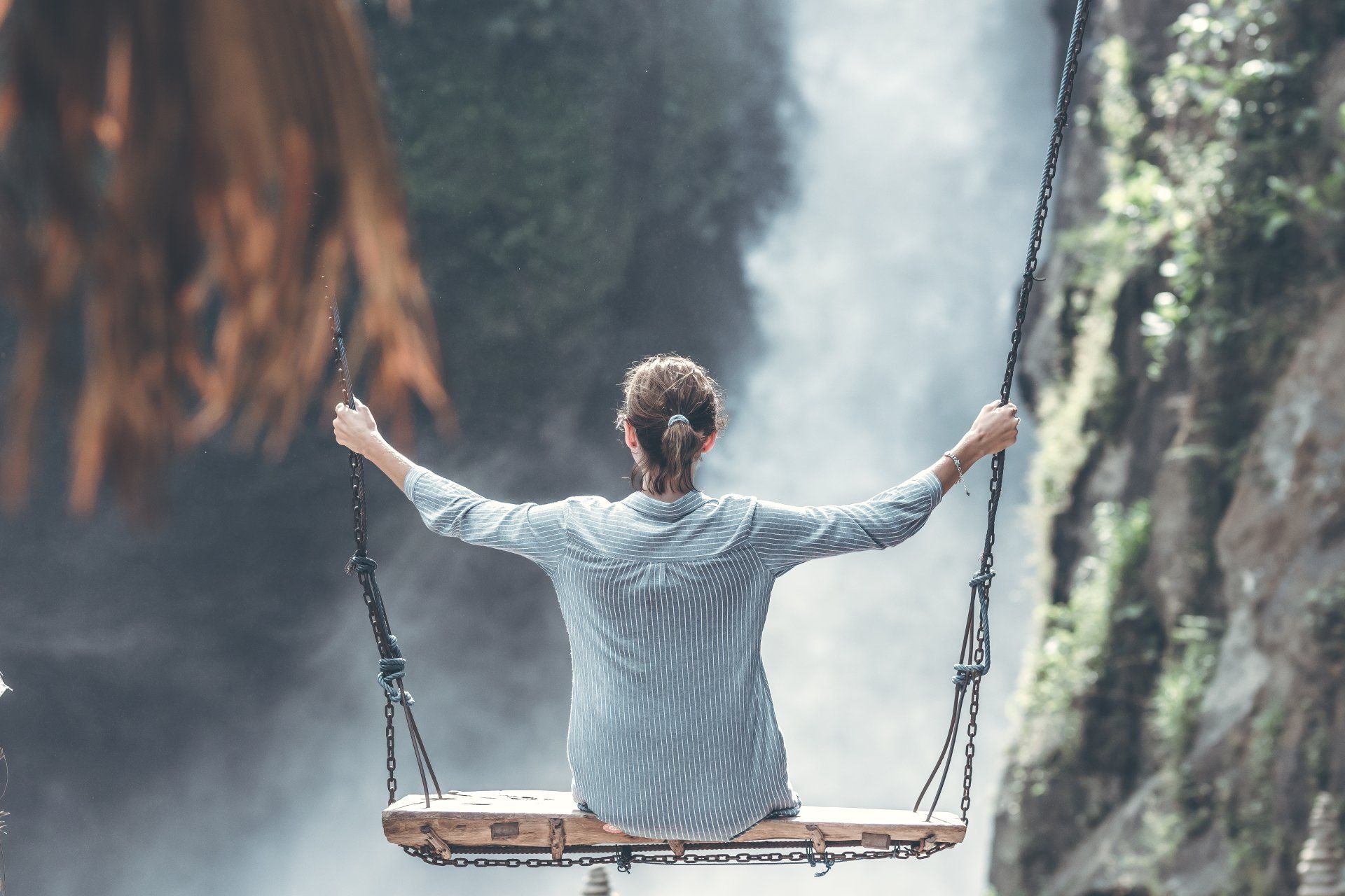 Eine Frau sitzt auf einer Schaukel vor einem Wasserfall.