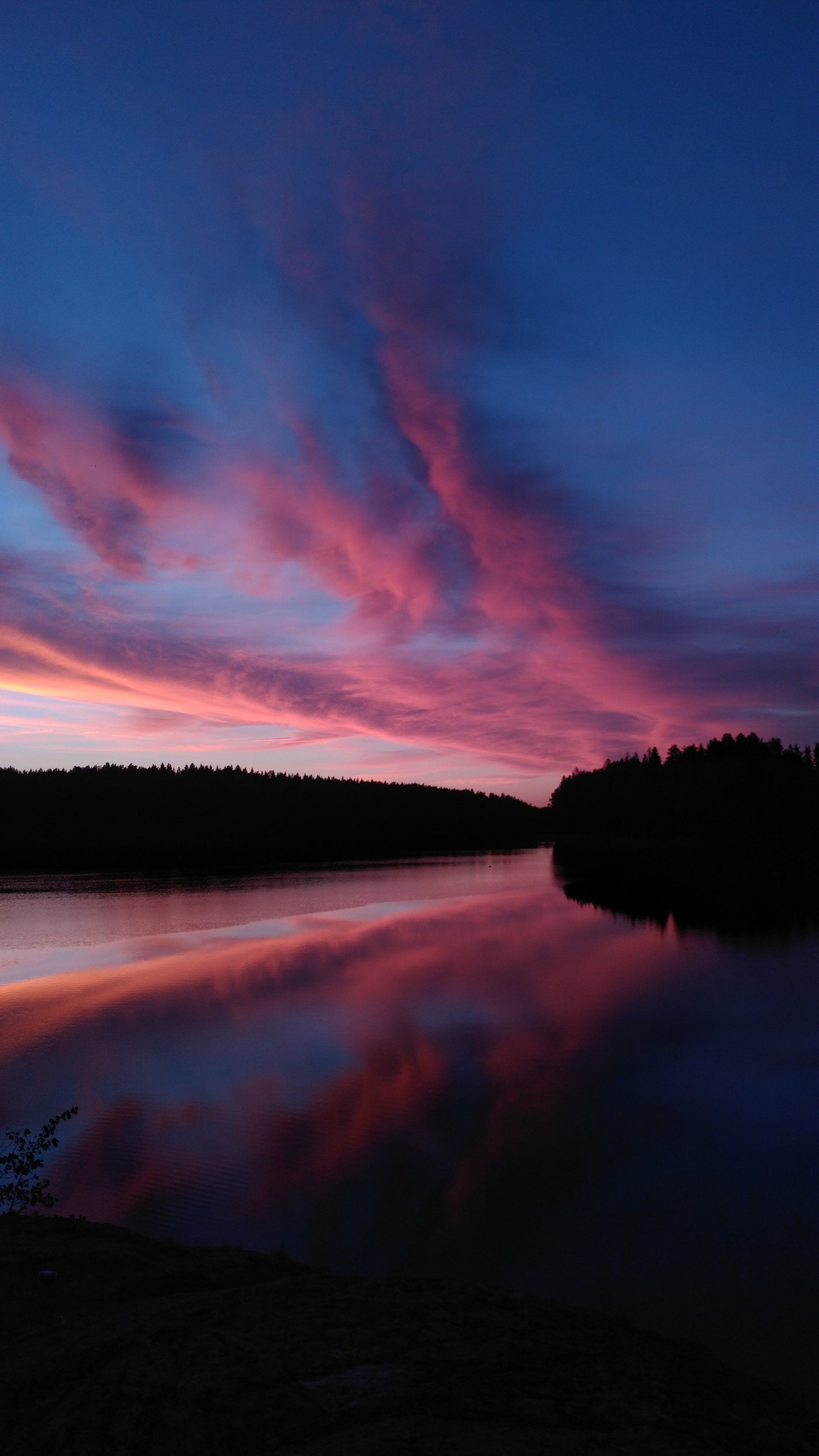 a lake with a sunset in the background and trees in the foreground .