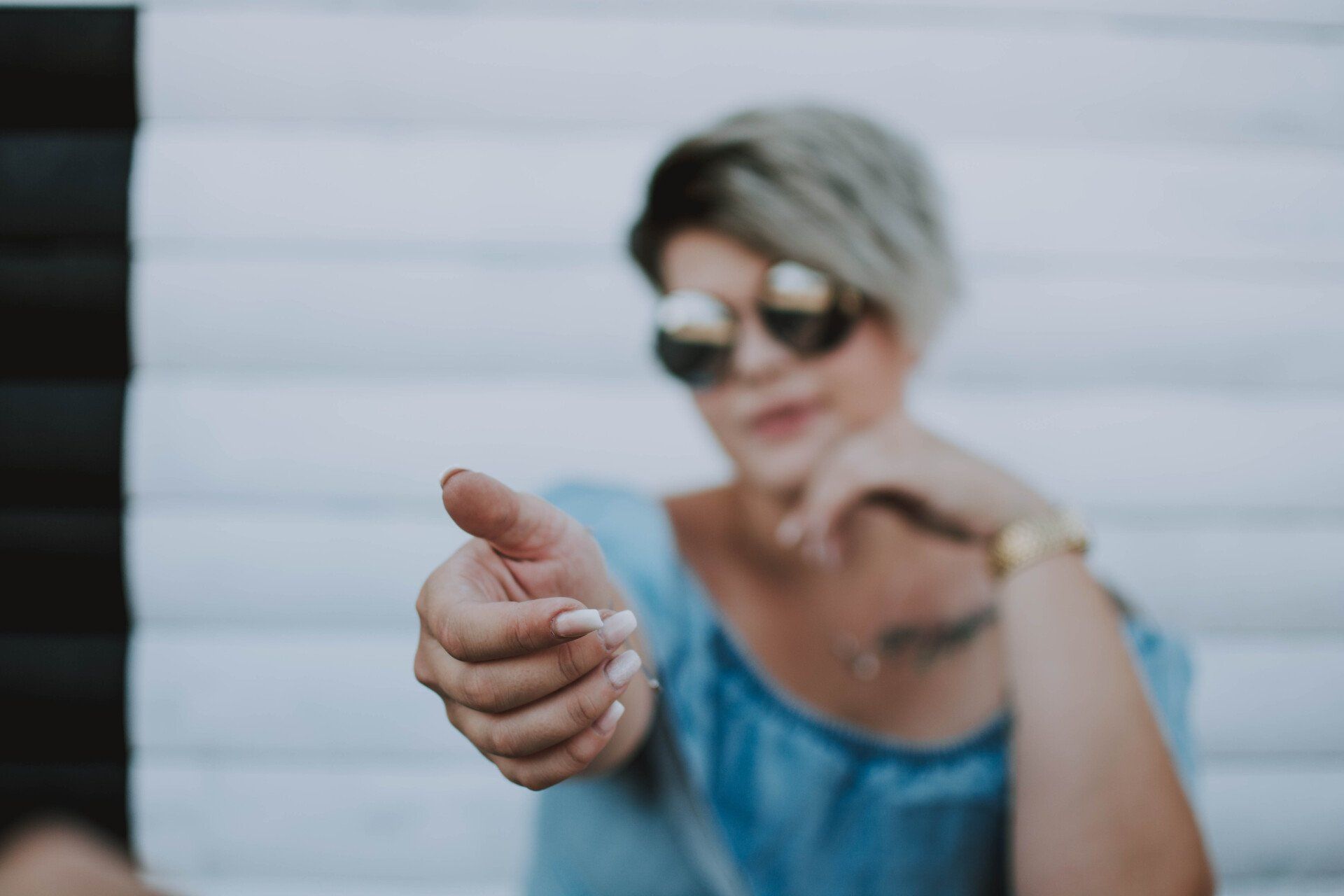 A woman wearing sunglasses is pointing at the camera.