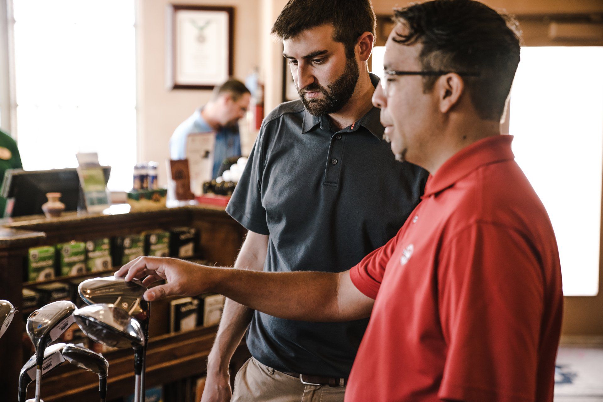 Two men are looking at a golf club in a store.