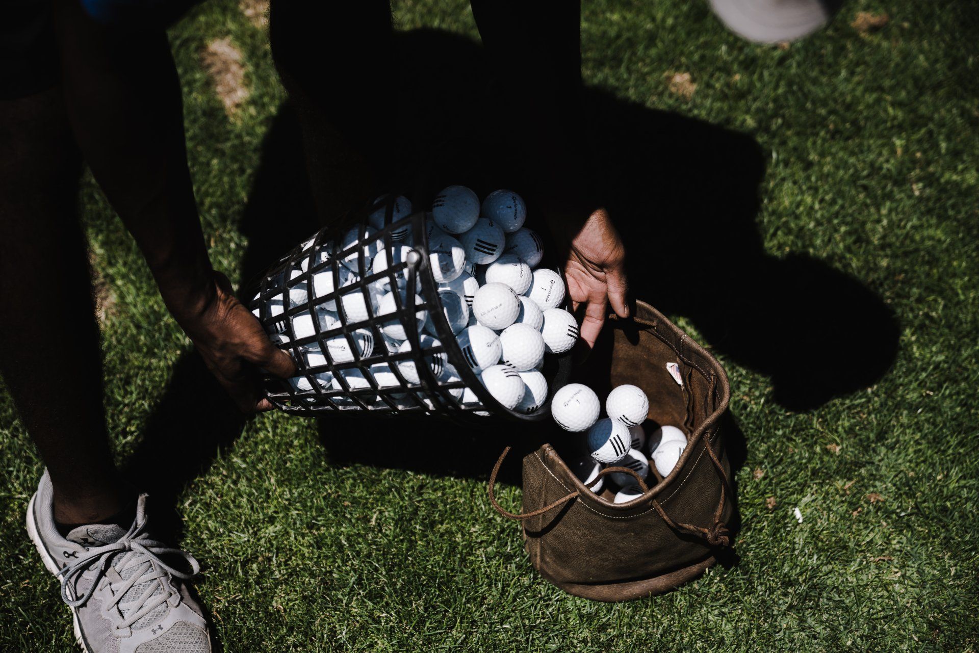 A person is holding a basket of golf balls at a driving range.