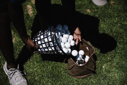 A person is holding a basket of golf balls at a driving range.