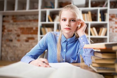 A young girl is sitting at a desk with a stack of books.