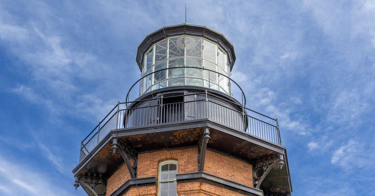 A lighthouse with a balcony on top of it against a blue sky.